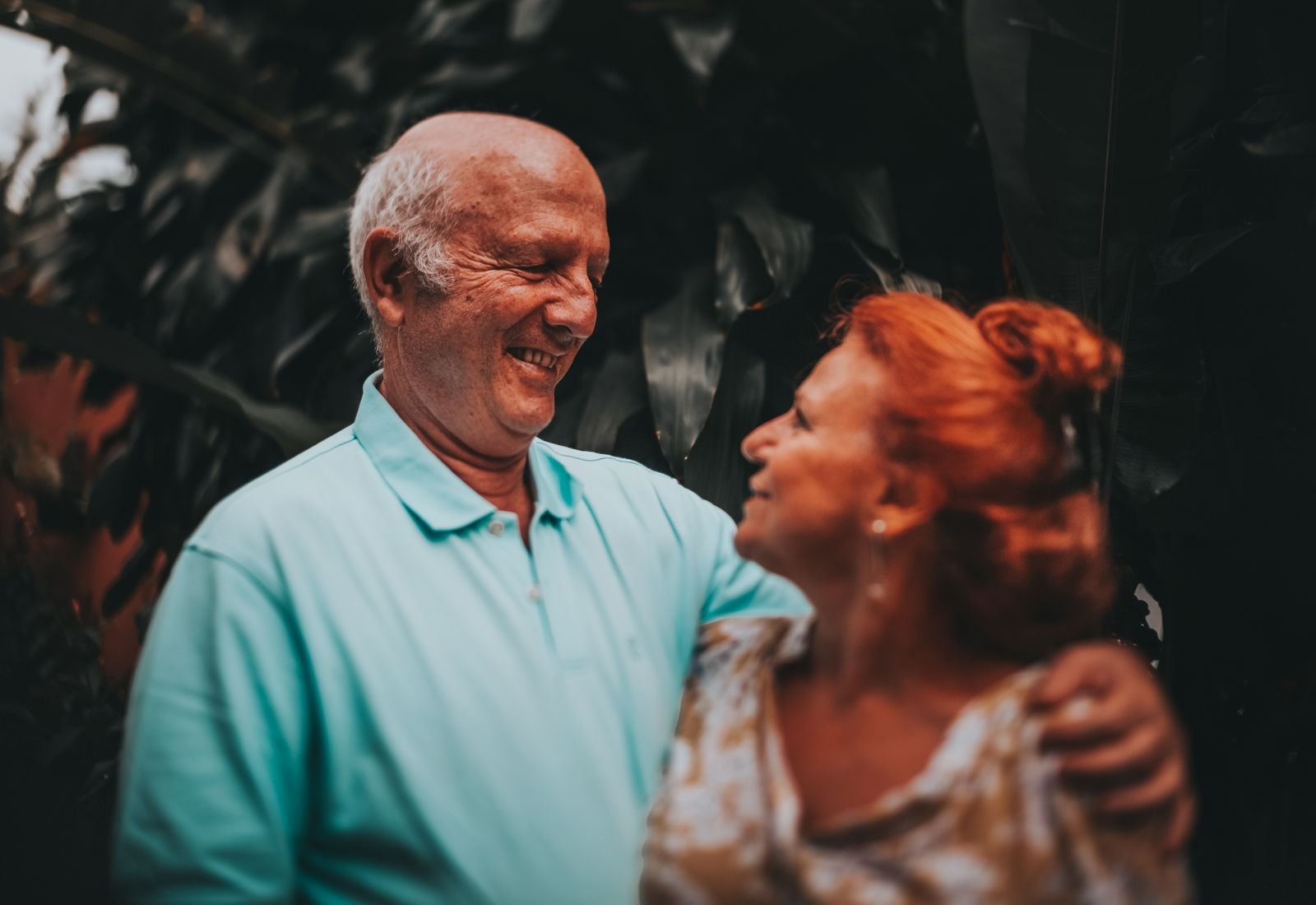 Casal de idosos sorrindo abraçado ao ar livre